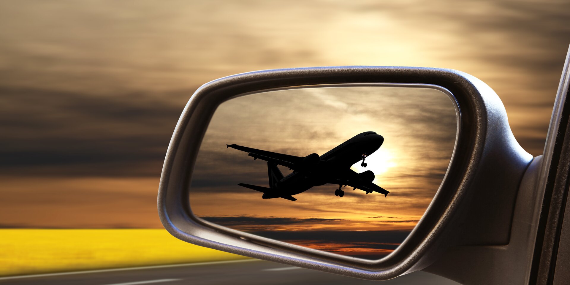 Airplane silhouette taking off reflected in car side mirror at sunset