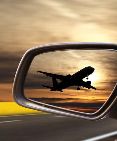 Airplane silhouette taking off reflected in car side mirror at sunset