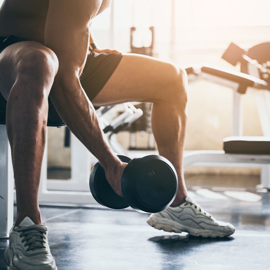 Mann sitzt auf Hantelbank und hebt eine Kurzhantel