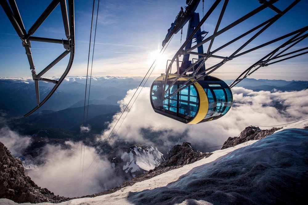 Cable car gondola suspended above snow and clouds on a mountain