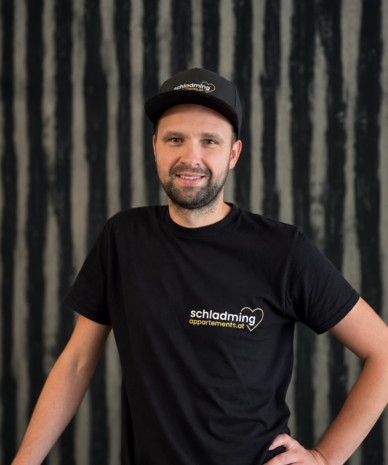 Smiling man in black shirt with schladming apartments.at logo