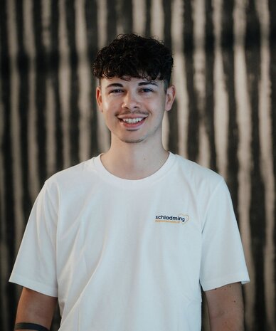 Lächelnder junger Mann in weißem T-Shirt mit schladming-Logo