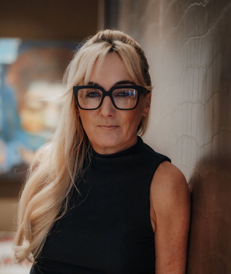 Woman with long blonde hair wearing black sleeveless top and glasses
