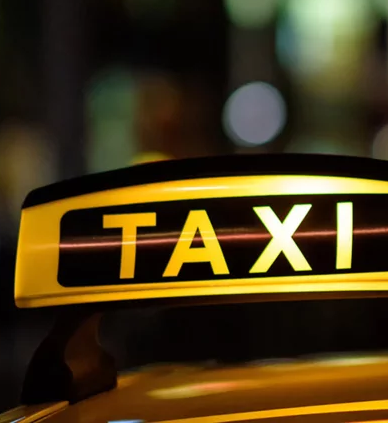 Taxi sign atop a car at night with city lights