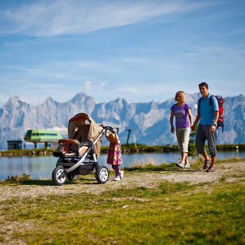 Family with stroller walking beside lake against mountains