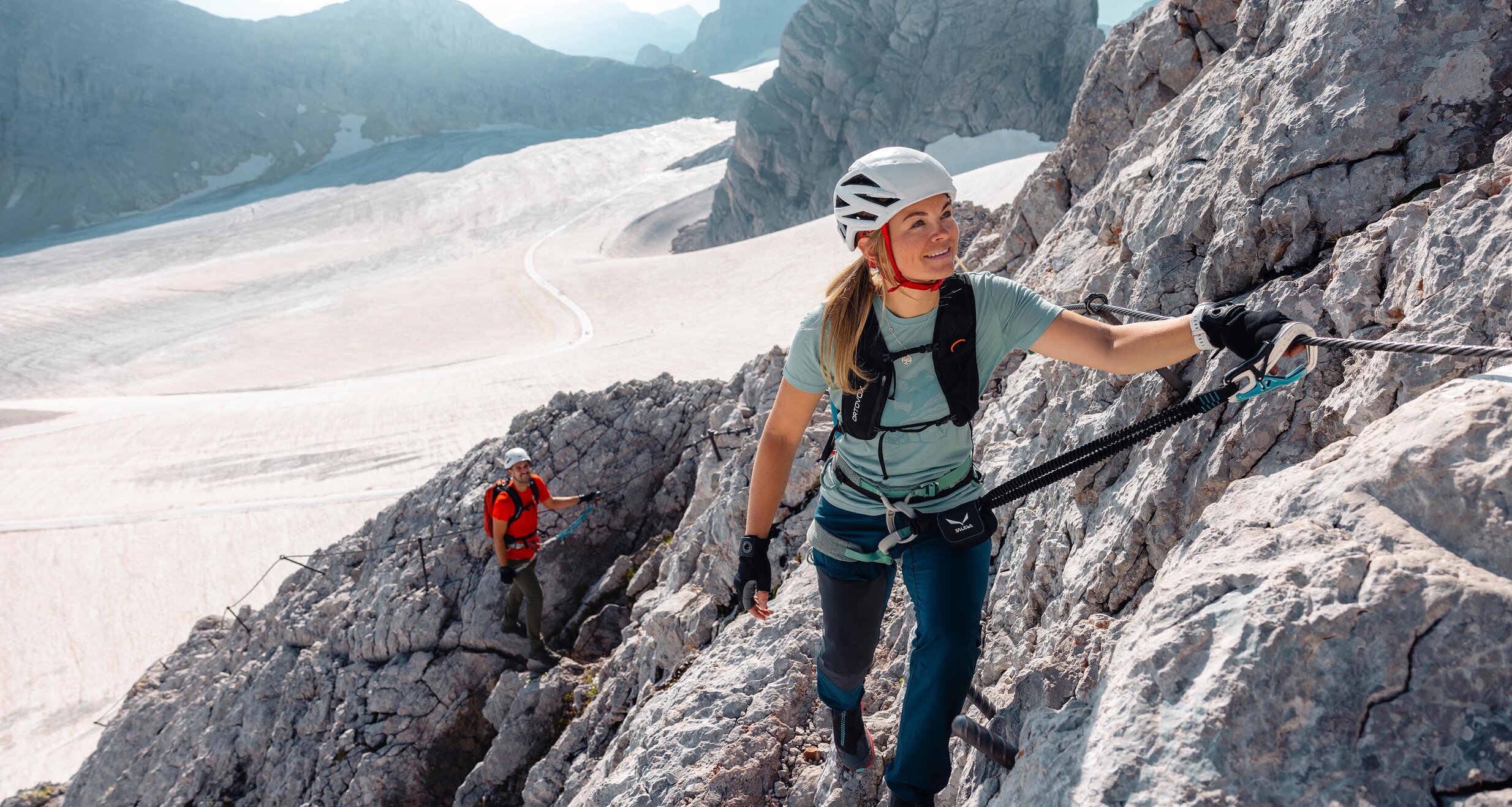 Two climbers ascend a snow-dusted mountain ridge with helmets