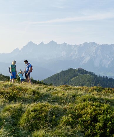 Family of three hiking on a grassy hillside with distant mountains