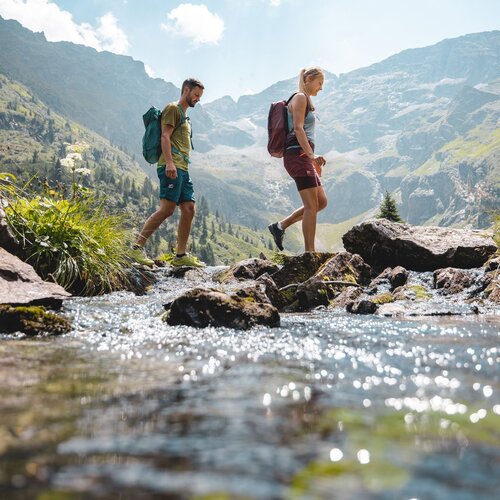 Two hikers crossing a rocky mountain stream with backpacks