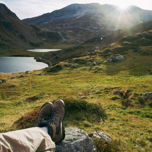 Hiker's legs and boots in foreground overlook alpine valley and lake