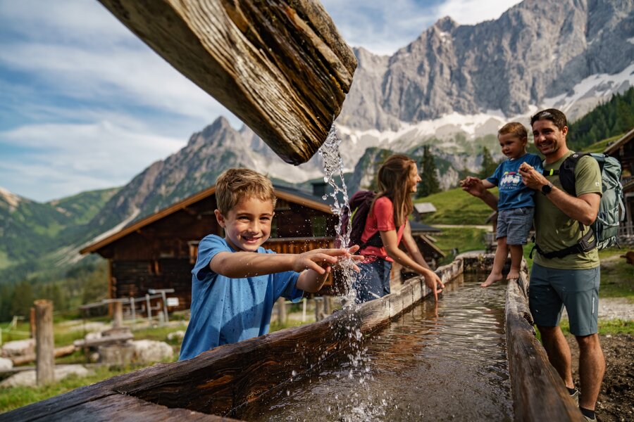 Smiling boy splashes water from a wooden trough | © Christine Höflehner