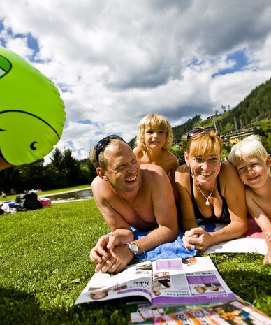 Family lying on grass by lake with green inflatable dinosaur nearby | © Tom Lamm