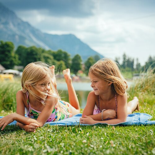 Two girls lying on a towel by a lake