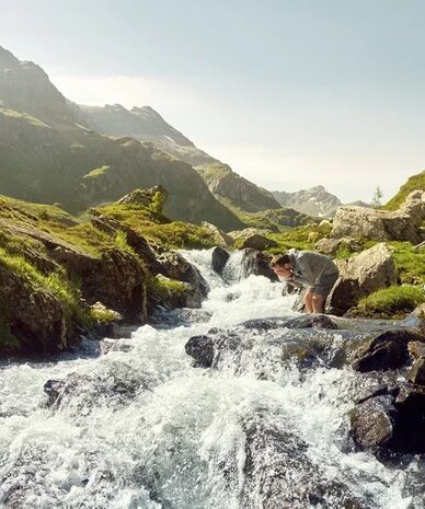 Two hikers by a rushing mountain stream in alpine terrain
