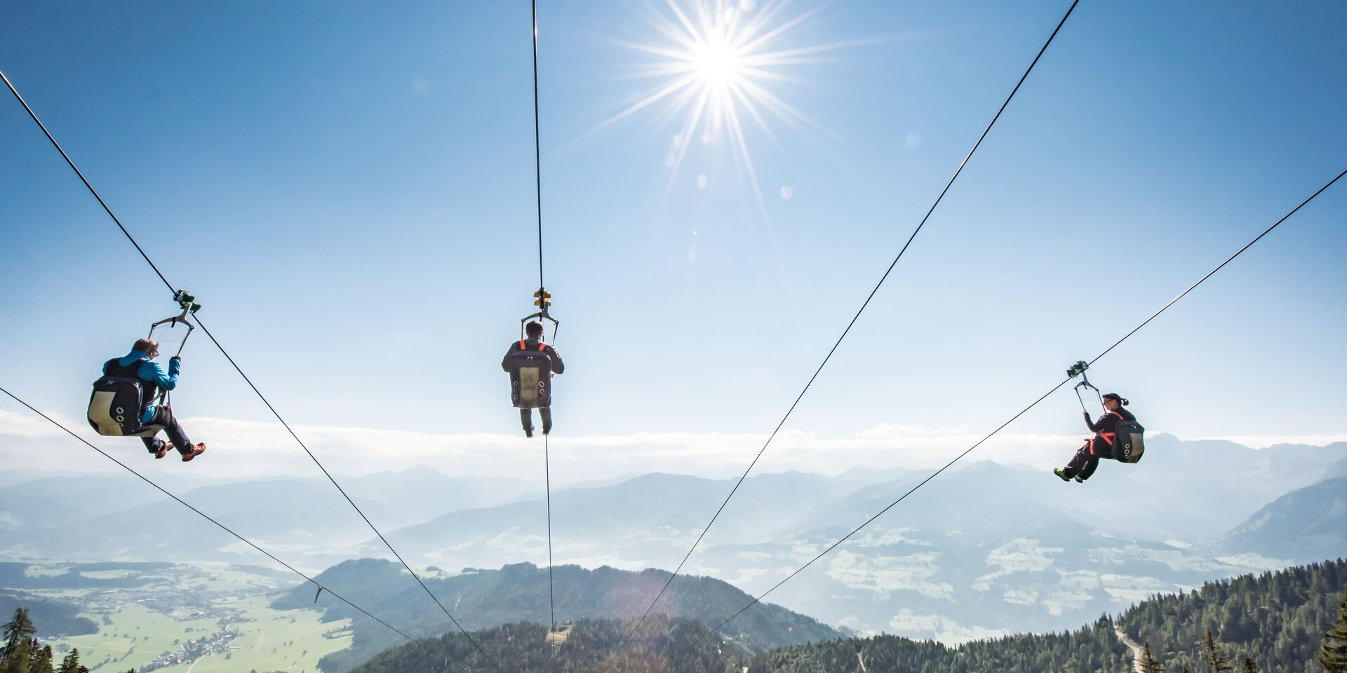 Three people zip lining over mountains under clear sky