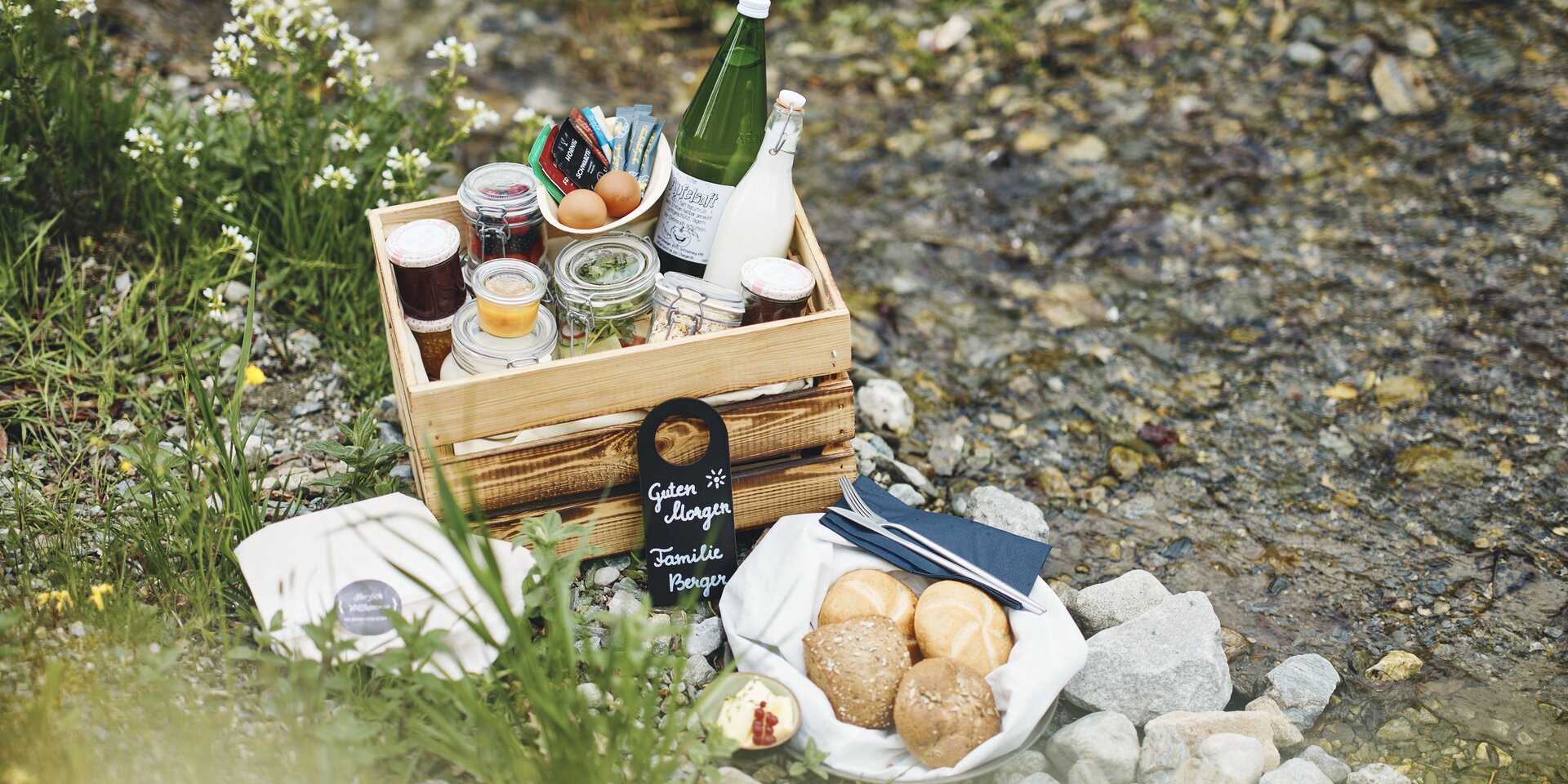Picnic setup beside a rocky stream with jars and bread. | © RAPHAELGABAUER.COM