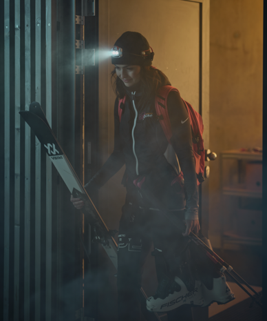 Frau mit Stirnlampe und Skiausrüstung hält Ski vor Tür