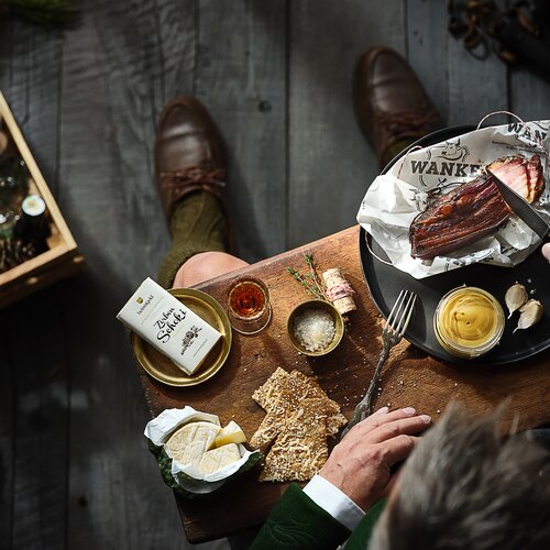 Top-down table with bread, cheese, butter, condiments, and meat plate | © RAPHAELGABAUER.COM
