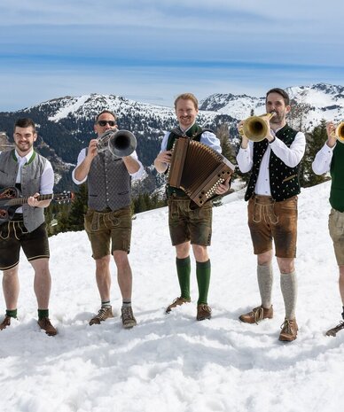 Group of Bavarian musicians playing outdoors in snowy mountains