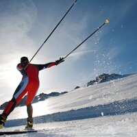 Skier in a red suit carving down a snowy slope with raised poles | © Leo Himsl