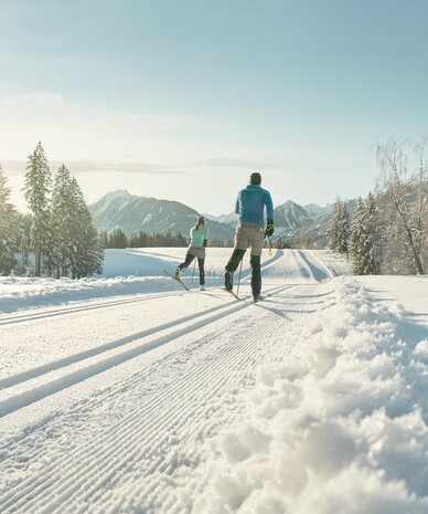 Zwei Skilangläufer auf schneebedeckter Strecke vor Berglandschaft | © Peter Burgstaller