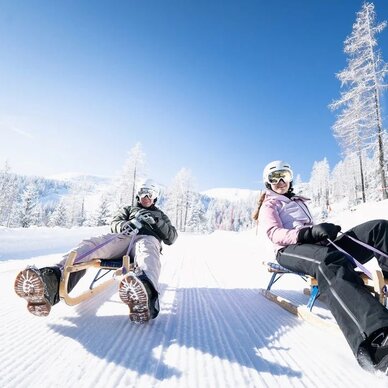 Two people sledding on wooden toboggans down a snowy slope
