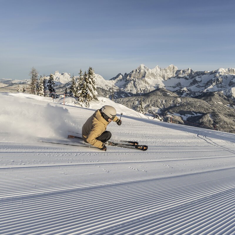 Skifahrer fährt Kurven auf präparierter Piste mit Bergkulisse | © Mirja Geh