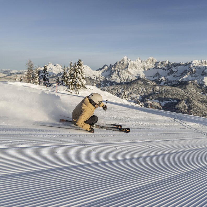 Skifahrer fährt Kurven auf präparierter Piste mit Bergkulisse | © Mirja Geh
