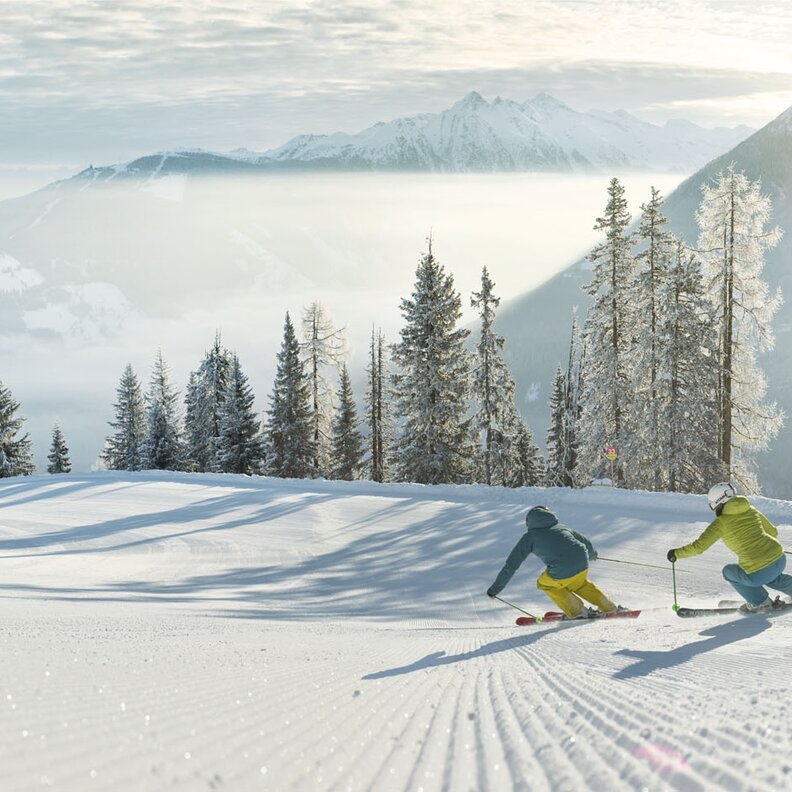 Zwei Skifahrer bahnen sich eine verschneite Abfahrt hinunter.