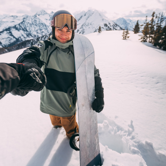 Snowboarder mit Snowboard vor schneebedeckter Berglandschaft