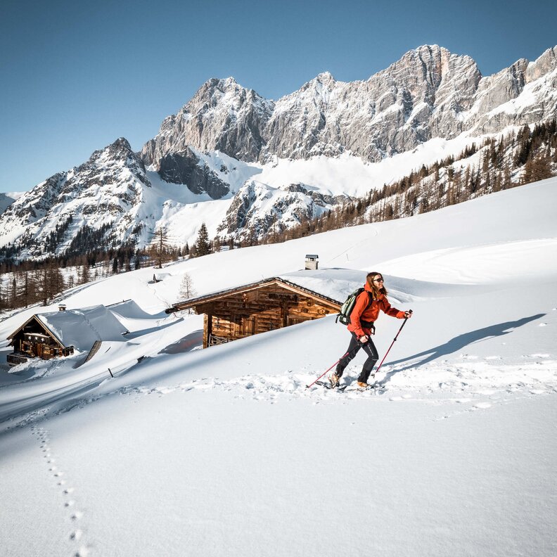 Schneebedeckte Alpenlandschaft mit Wanderer und Holzhütten