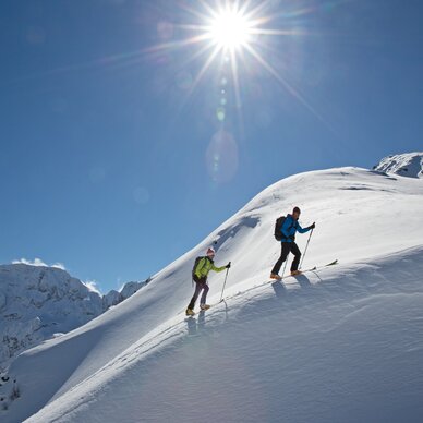 Zwei Bergsteiger erklimmen verschneiten Berghang bei hellem Sonnenschein. | © HERBERT RAFFALT