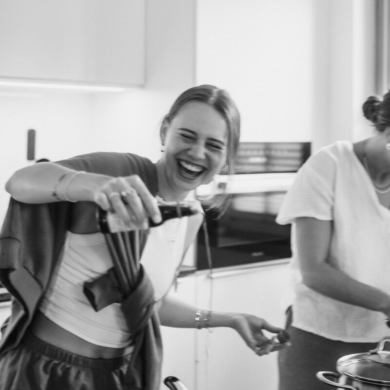 Frau lacht, während sie Zutaten in eine Pfanne gießt