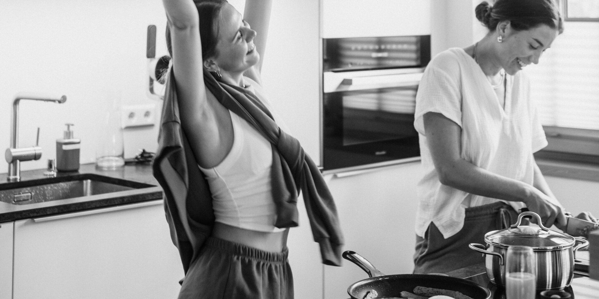 Two women in a bright modern kitchen; one raises arms.