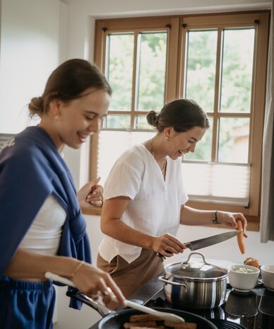Zwei Frauen kochen in heller Küche, schneiden und braten