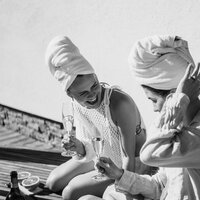 Zwei Frauen mit Handtüchern auf dem Kopf stoßen mit Sekt an.