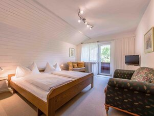 Bright hotel bedroom with large bed, seating area, and balcony door