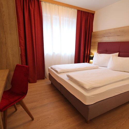 Hotel bedroom with a double bed, red headboard, and wooden furniture.