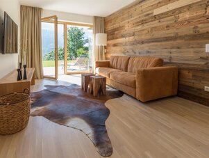 Wohnzimmer mit braunem Sofa, Holzwand und Terrassentüren.