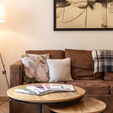 Gemütliches Wohnzimmer mit braunem Sofa, Couchtischen und Kunst.