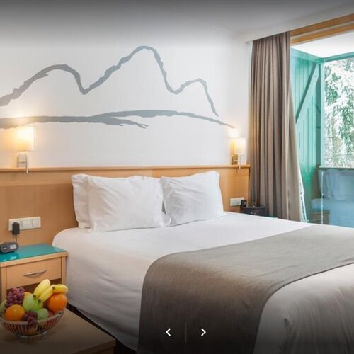 Hotel room with large bed, wall mural, and glass doors to balcony.