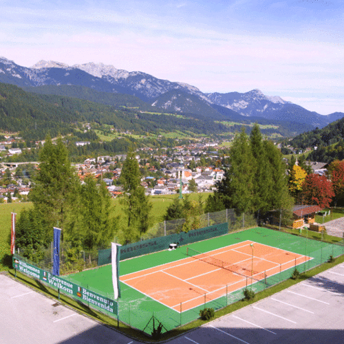 Outdoor clay tennis court with surrounding mountains and town