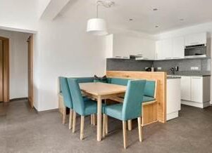 Open-plan kitchen and dining area with teal chairs around a wooden table