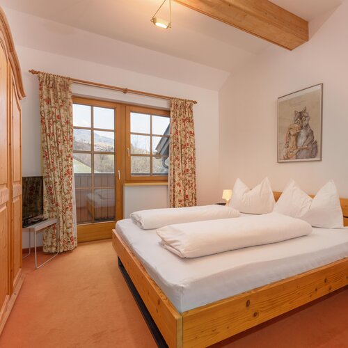 Gemütliches Schlafzimmer aus Holz mit großem Bett, Kleiderschrank und floralen Vorhängen