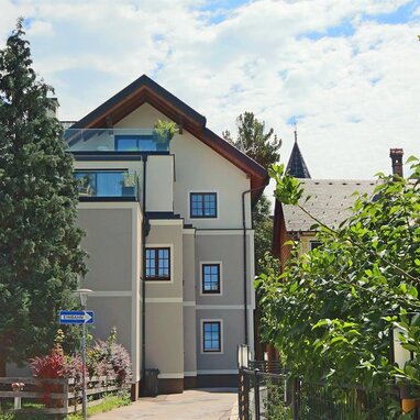 Three-story apartment building with trees and a one-way sign.