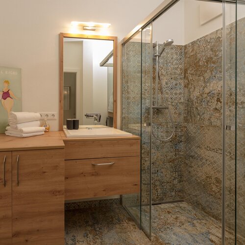 Wooden bathroom vanity with sink, towels stacked nearby and glass shower
