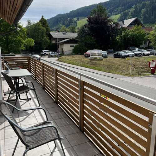 Balcony with wooden railing and chairs overlooking street and hillside