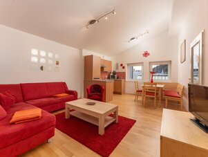 Helles Wohnzimmer mit rotem Sofa, Essbereich und Küche.