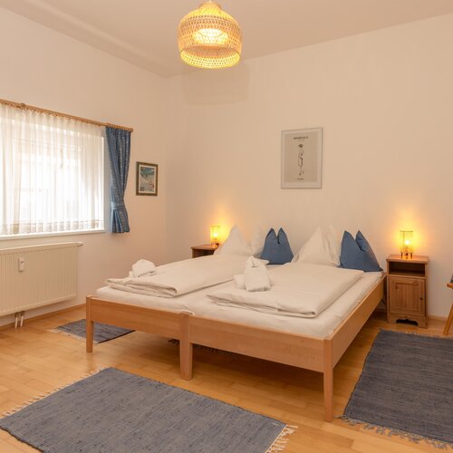 Helles Schlafzimmer mit Doppelbett, blauen Kissen und Vorhängen