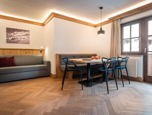 Wohnzimmer mit Sofa, Esstisch und Stühlen vor großem Fenster