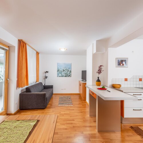 Open-plan living area with gray sofa, orange curtains, and kitchen island.